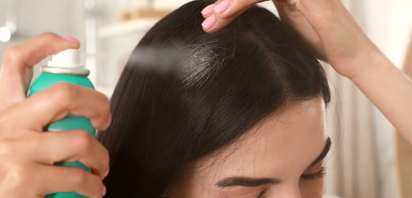 Woman applying dry shampoo onto her hair indoors, closeup.